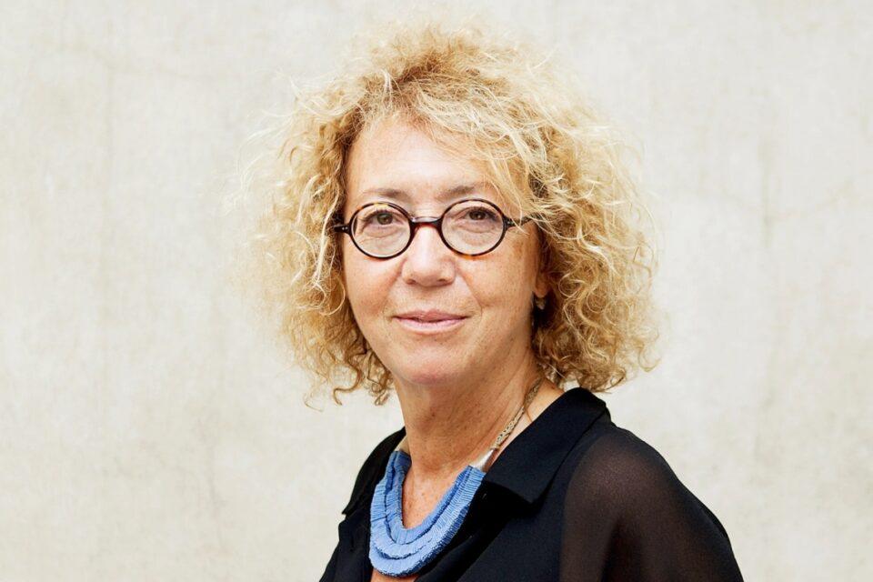 مصورة فنية عصرية ذات شعر مجعد وعيون لابسة نظارات أنيقة، ترتدي ملابس سوداء وإكسسوارات فريدة.